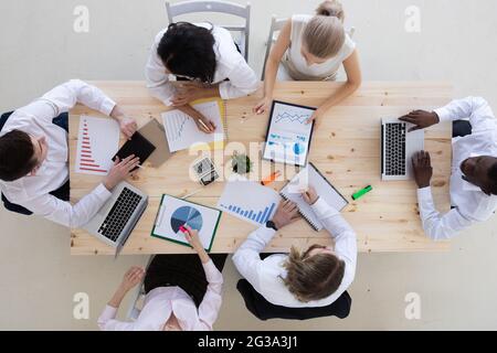 Geschäftsleute, die bei einem Treffen am Holztisch im Büro mit einem Laptop, Geschäftszusammenfassungen, Vertrags- und Versicherungsunterlagen arbeiten. Teamarbeit Stockfoto