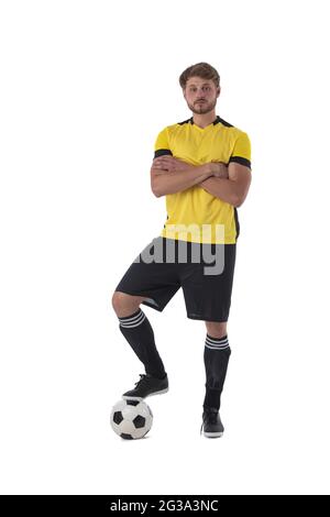 Fußballspieler, der mit einem Fuß auf einem Ball steht und Arme kreuzt, isoliert auf weißem Hintergrund Stockfoto