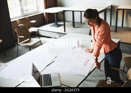 Junge fröhliche Brünette weibliche Business-Analyst in Brillen arbeiten mit Dokumenten und Laptop Stockfoto