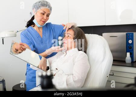 Weibliche Kosmetologin, die in der Klinik auf der Couch liegende reife Patientin konsultiert Stockfoto