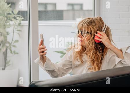 Ältere oder Erwachsene Frau zu Hause, die Musik mit Mobiltelefon und Kopfhörern hört Stockfoto