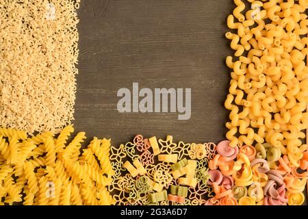 Rohe Pasta in verschiedenen Farben, Typen und Größen auf einem dunklen Holztisch ausgelegt Stockfoto