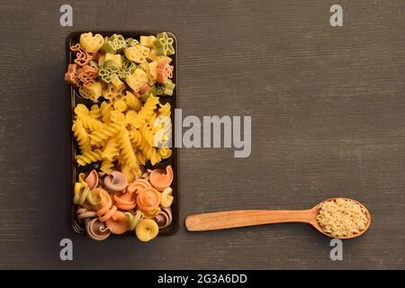 Rohe Nudeln verschiedener Farben, Typen und Größen werden in einer Schachtel angelegt und daneben liegt ein Löffel mit Vermicelli. Es gibt einen Platz für eine Inschrift Stockfoto