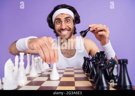 Foto von jungen glücklich fröhlich lächelnd funky Geek Nerd Mann in Brille spielen Schach isoliert auf violettem Hintergrund Stockfoto