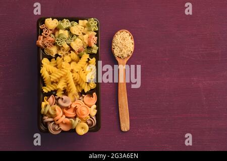 Rohe Nudeln verschiedener Farben, Typen und Größen werden in einer Schachtel angelegt und daneben liegt ein Löffel mit Vermicelli. Richtige Stelle für Text Stockfoto