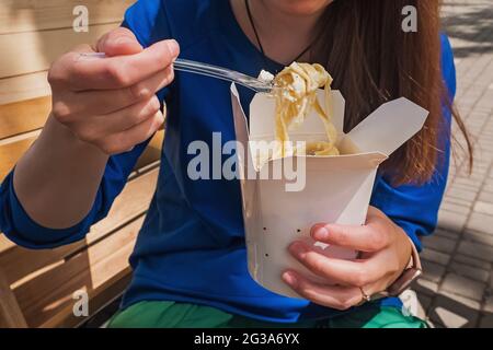 Nahaufnahme einer Frau, die Tagliatelle-Pasta aus einem Papierkarton isst. Stockfoto