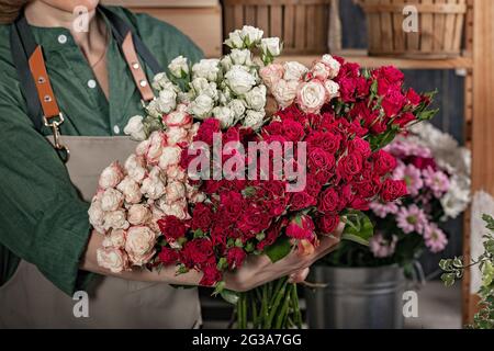 Frau Floristin hält einen großen Strauß Rosen. Floristen-Arbeitsplatz. Konzept für kleine Unternehmen. Blumen und Accessoires Shop. Nahaufnahme Stockfoto