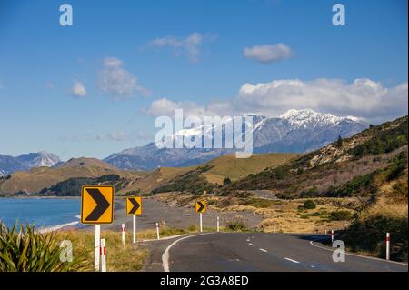 State Highway 1, eine berühmte Küstenstraße in der Nähe von Kaikoura, Neuseeland, eine der besten Küstenstraßen der Welt. Schneebedeckte Berge, Meer, Himmel und Straße Stockfoto