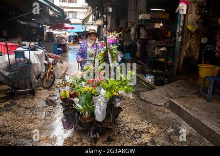 Ein Straßenhändler schiebt ihren Wagen mit frischen Blumen durch den nassen Markt im Bang Rak-Viertel von Bangkok, Thailand. Stockfoto