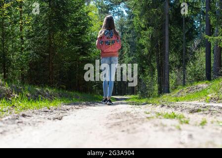 Ein junges Mädchen mit Rucksack zu Fuß entlang Weg durch den Wald während des Sommers. Hipster Lifestyle und Solo Trip.Rückansicht. Stockfoto