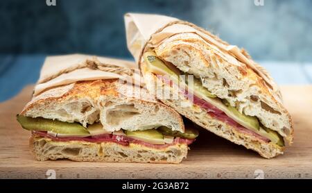 Ciabatta-Sandwich mit knuspriger Kruste, Senf, Schinken, Käse, Gurken auf einem Holztablett Stockfoto
