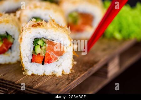 Katsuobushi Uramaki Sushi Roll mit Lachs und Gurke auf Holzbrett auf schwarzem Hintergrund. Sushi-Rolle mit trockenen Fischbonito-Flocken Stockfoto