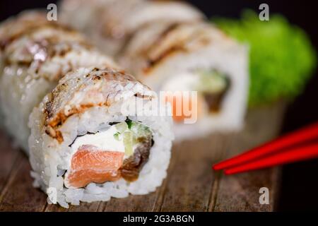 Uramaki Sushi-Rolle mit Lachsfisch, Avocado und Frischkäse philadelphia, Sushi-Rolle mit gebranntem Fischfilet auf Holzbrett auf schwarzem Backgro bedeckt Stockfoto