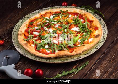 Nahaufnahme Pizza Margherita mit Buffalo Mozzarella, Tomaten und frischem Basilikum. Pizzaschneider liegt auf dem Holzhintergrund. Traditionelles italienisches Fast Food Stockfoto