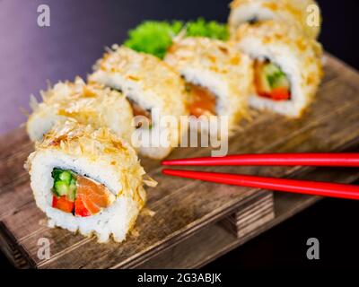 Katsuobushi Uramaki Sushi Roll mit Lachs und Gurke auf Holzbrett auf schwarzem Hintergrund. Sushi-Rolle mit trockenen Fischbonito-Flocken Stockfoto