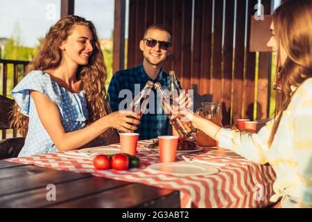 Junge Freunde haben Spaß, trinken Getränke zu Hause Abendessen im Freien, glückliche Menschen essen gemeinsam Grill in der Natur, bei Sonnenuntergang Stockfoto