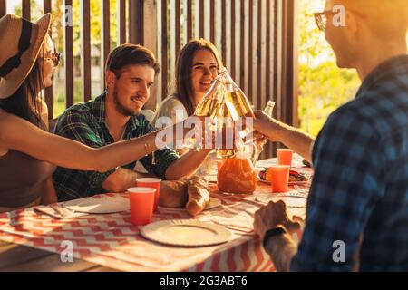 Eine Gruppe von Freunden, jungen Männern und Frauen beim Grillen in der Natur, glückliche Menschen sitzen am Tisch und essen, Spaß beim Picknick, Sommerzeitkonzept Stockfoto