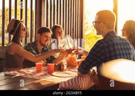 Eine Gruppe von Freunden, jungen Männern und Frauen beim Grillen in der Natur, glückliche Menschen sitzen am Tisch und essen, Spaß beim Picknick, Sommerzeitkonzept Stockfoto