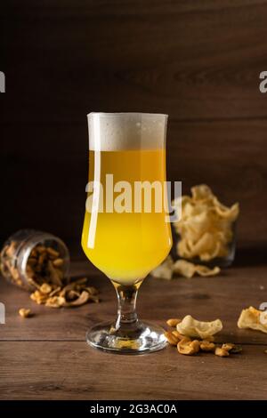 Helles Bier ungefiltert mit einem großen starken weißen Schaum auf einem Holzhintergrund, Copyspace. Mit Bier-Snacks Stockfoto
