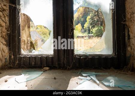 Altes kaputtes, dreckiges Fenster an einer alten Wand mit rissigem Putz und abblätternder Farbe Stockfoto