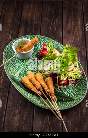 Garnelen Tempura mit frischem Salat auf dem grünen Teller mit einem Muster. Brauner Hintergrund aus Holz. Traditionelle japanische Küche. Stockfoto