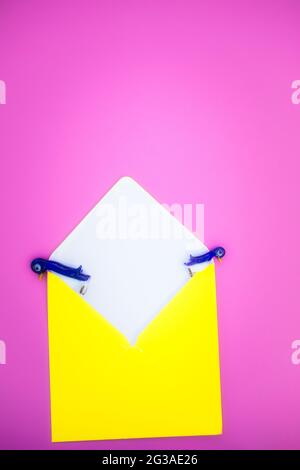 Zwei niedliche Pinguin-Figuren aus Glas, die über die Seiten des gelben Umschlags auf rosa Hintergrund gucken. Konzept der Kontemplation, Flucht, Stockfoto