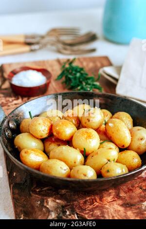 Goldene Babykartoffeln in gusseiserner Pfanne auf Holzbrett mit Kräutern und Salz rösten Stockfoto