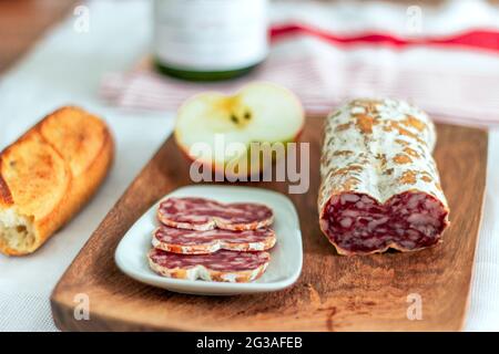 Fleischplatte mit Salami, knusprigem Baguette-Brot, Apfel und Wein auf einem Holzbrett Stockfoto