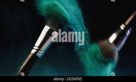 Verschwommene kosmetische Pinsel mit leuchtend türkisfarbener holi-Farbe, die auf schwarzem Hintergrund spritzt Stockfoto