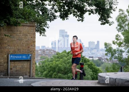 Mit den Wolkenkratzern der City of London, dem Finanzviertel der Hauptstadt, in der Ferne überquert ein Läufer am 15. Juni 2021 den Sydenham Hill im Süden Londons, England. Stockfoto