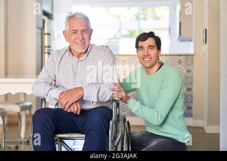 Zufriedener Senior im Rollstuhl und Pflegepersonal zu Hause oder im Seniorenheim Stockfoto