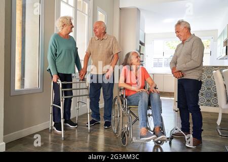 Gruppe von Senioren mit Rollstühlen und Gehrahmen im Gespräch im Altersheim Stockfoto