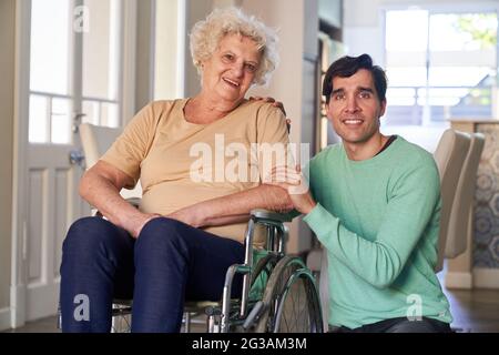 Zufriedener älterer Bürger im Rollstuhl mit ihrem Sohn oder Ehemann von der häuslichen Pflege Stockfoto