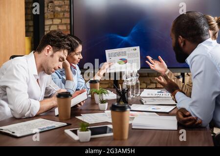 afroamerikanische Geschäftsfrau, die Dokumente mit Analysen in der Nähe von multiethnischen Kollegen hält Stockfoto