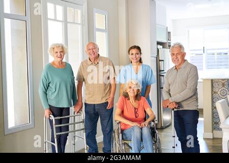 Gruppe von Senioren mit Rollstühlen und Gehrahmen im Altersheim, die von einer geriatrischen Krankenschwester betreut werden Stockfoto