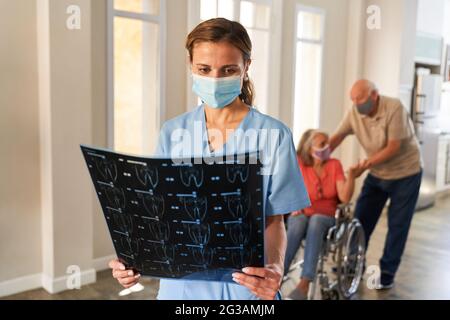 Arzt mit Gesichtsmaske wegen Covid-19 betrachtet ein MRT-Bild in der oberen Rehabilitationsklinik Stockfoto