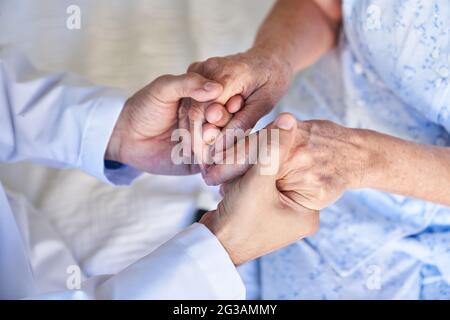 Eine geriatrische Krankenschwester oder ein Arzt hält die Hände eines älteren Bürgers als Symbol für Unterstützung und Komfort Stockfoto