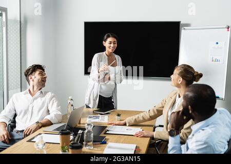 Schwanger afroamerikanische Geschäftsfrau lächelt, während sie mit multiethnischen Kollegen spricht Stockfoto