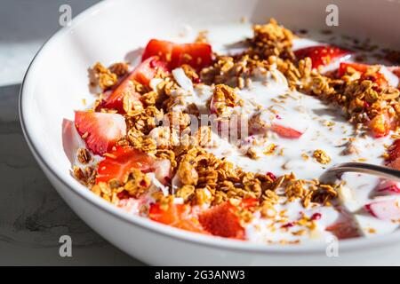 Müsli mit Joghurt und Erdbeeren in einer weißen Schüssel, Nahaufnahme. Gesundes Frühstückskonzept. Stockfoto