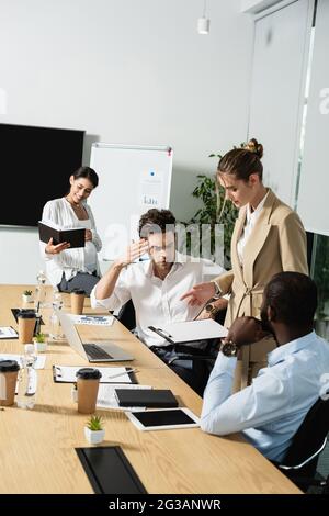 Geschäftsfrau, die auf die Zwischenablage in der Nähe multiethnischer Geschäftspartner zeigt Stockfoto