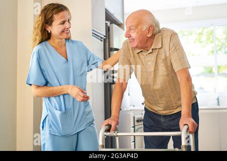 Freundliche Pflegekraft, die sich in einer Rehabilitationsklinik oder in einem Pflegeheim um Senioren mit Gehrahmen sorgt Stockfoto
