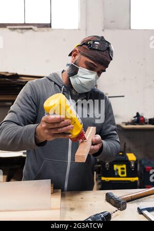 Zimmermann mit Maske, der Leim auf ein Holzbrett setzt Stockfoto