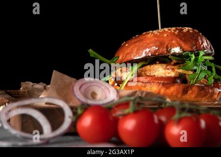 Großer amerikanischer Burger auf schwarzem Hintergrund. Cutlet mit Käse, Tomate, Huhn und Rucola auf einem Holztablett, Kopierraum, Nahaufnahme Stockfoto