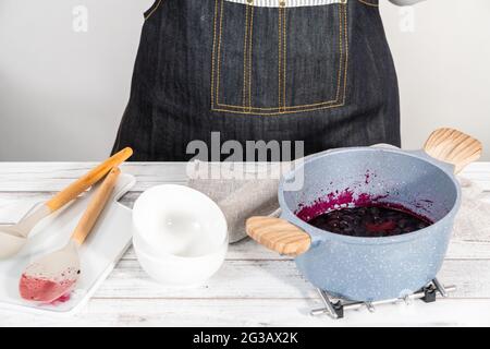 Gemischtes Beerenkompott aus gefrorenen Beeren in einem antihaftbeschichteten Kochtopf zubereiten. Stockfoto