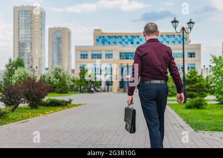 Ein Mann mit Aktentasche, der in einem Bürogebäude arbeiten wird. Rückansicht des Büromitarbeiters, der mit einer Aktentasche zur Arbeit geht Stockfoto
