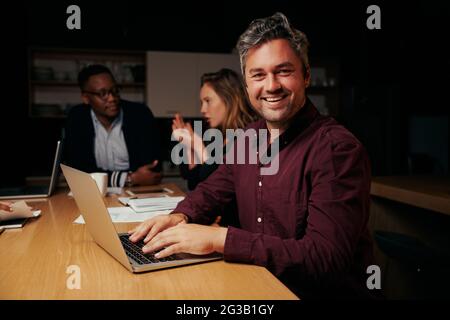 Porträt eines erfolgreichen männlichen Geschäftsführers, der mit seinem Team im Büro einen Laptop verwendet Stockfoto