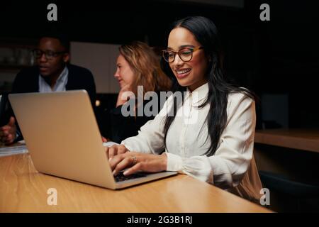Porträt einer lächelnden jungen Geschäftsfrau, die in der Nähe von Kollegen sitzt, die im Büro am Laptop arbeiten Stockfoto