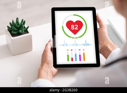Unkenntliche Frau, die die neueste Gesundheitsanwendung auf einem digitalen Tablet verwendet, während sie im Büro arbeitet, ihre Herzfrequenz überprüft und über die Schulter geschossen wird. Healthcar Stockfoto