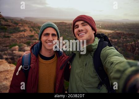 Portrait von gutaussehenden männlichen Freunden, die Selfie mit Rucksack machen, während sie den Berg besteigen Stockfoto