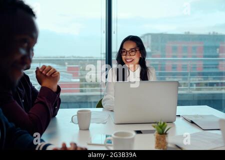 Erfolgreiche lächelnde junge Frau, die bei einem Geschäftstreffen mit seinen multiethnischen Kollegen sitzt Stockfoto